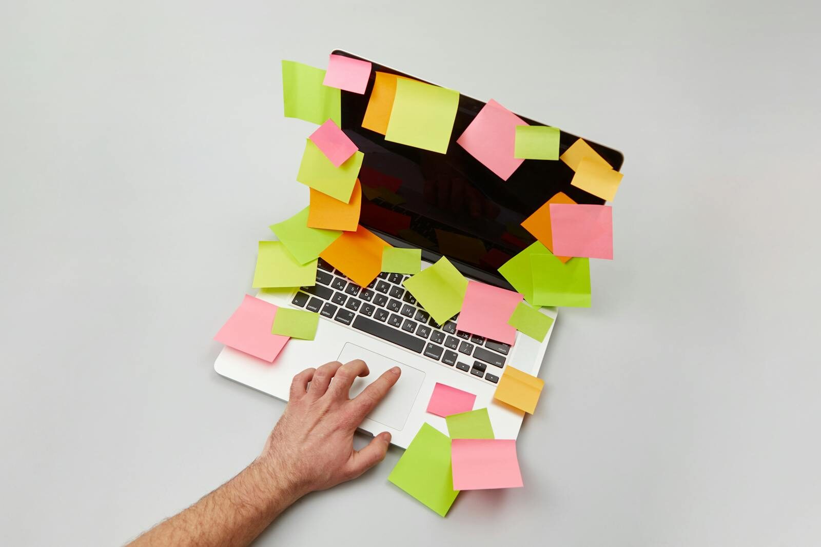 Hand on laptop surrounded by colorful sticky notes, depicting a busy and organized workspace.
